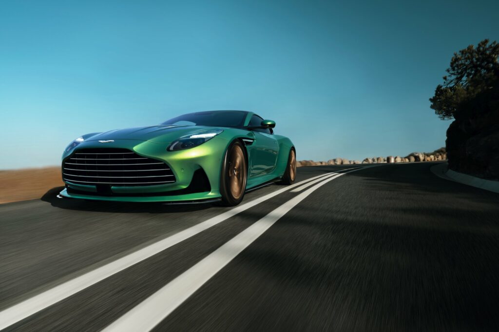 zielony Aston Martin DB12 jadący po pustej, krętej drodze