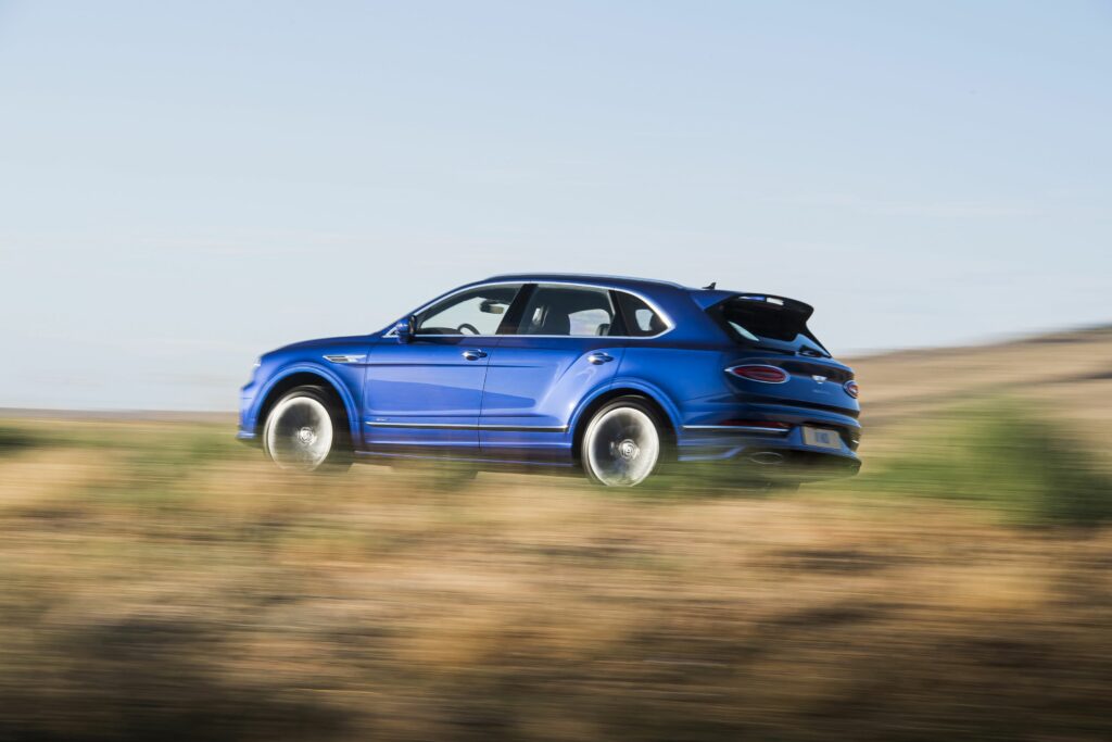 niebieski Bentley Bentayga Speed jedzie szybko po drodze wśród traw