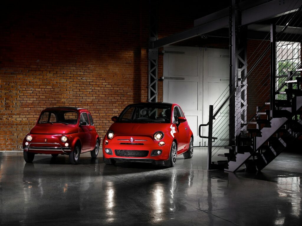 Czerwony pierwszy Fiat 500 i czerwony nowy Fiat 500 stojące w industrialnym wnętrzu