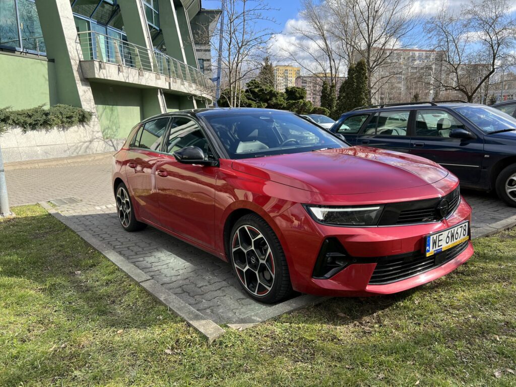 czerwony Opel Astra stojący na parkingu pod blokiem