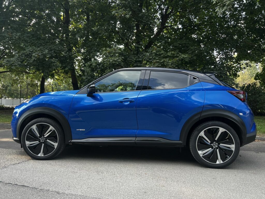 niebieski Nissan Juke stoi na drodze wśród drzew
